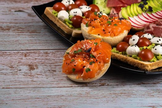 Assorted sandwiches with fish, cheese, meat and vegetables on a black plate.