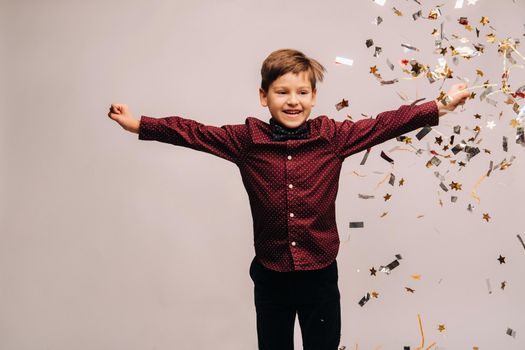 Beautiful boy jumping for joy and with confetti on a gray background.