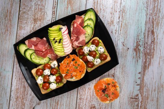 Assorted sandwiches with fish, cheese, meat and vegetables on a black plate.