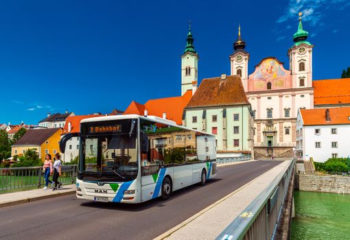 Steyr - June 2020, Austria: View of the Steyr Bridge with a modern bus, walking girls, and St. Michael's Church behind