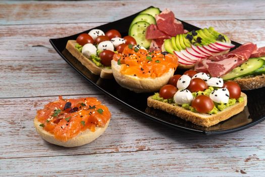 Assorted sandwiches with fish, cheese, meat and vegetables on a black plate.