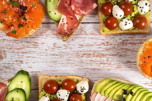 An assortment of sandwiches with fish, cheese, meat and vegetables lay on the wooden table.