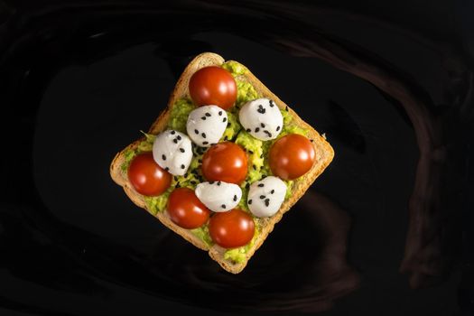 A cheese and tomato sandwich sits in a black plate on a wooden background.