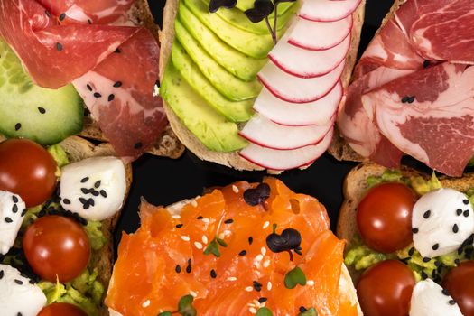 Assorted sandwiches with fish, cheese, meat and vegetables on a black plate.