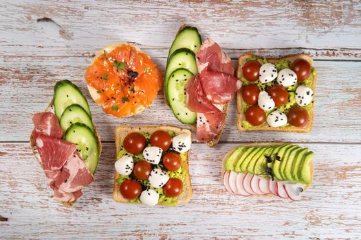 An assortment of sandwiches with fish, cheese, meat and vegetables lay on the wooden table.