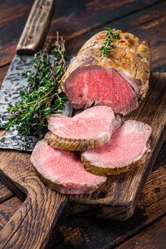 Roast Tenderloin beef fillet meat on a wooden board with herbs. Dark wooden background. Top view.