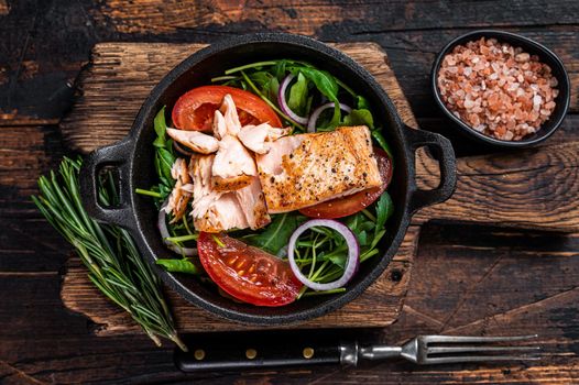 Grilled salmon fish fillet steak with fresh salad arugula, avocado and tomato in a pan. Dark wooden background. Top view.