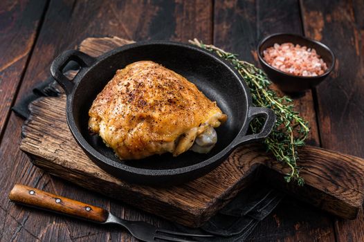 Baked chicken thigh in a pan with rosemary and salt. Dark wooden background. Top View.