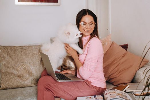 a girl in pajamas at home is working on a laptop with her dog Spitzer, the dog and its owner are resting on the couch and watching the laptop.Household chores.