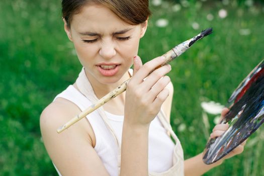 Woman in white dress with palette of paints on nature art drawing. High quality photo