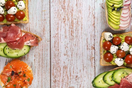 An assortment of sandwiches with fish, cheese, meat and vegetables lay on the wooden table.