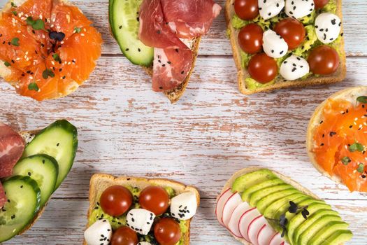 An assortment of sandwiches with fish, cheese, meat and vegetables lay on the wooden table.