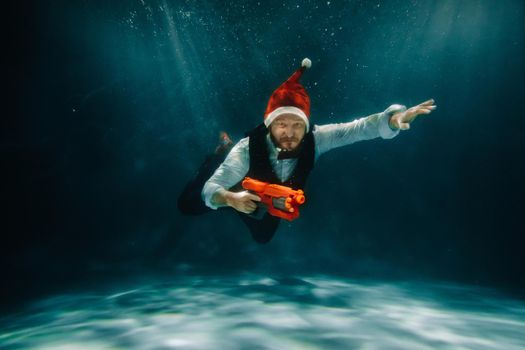 A man under water in a suit and a red gun in his hands. Santa Claus is swimming underwater with a gun.Christmas concept.