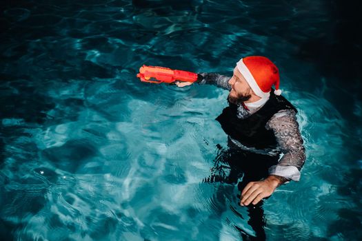 A man in a Santa Claus suit and hat with a red gun in his hands. Santa Claus is swimming underwater with a gun.Christmas concept