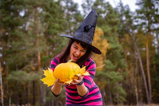 attractive witch with pumpkin in the autumn forest. halloween party concept