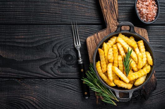 Fried Crinkle French fries potatoes in a pan. Black Wooden background. Top view. Copy space.