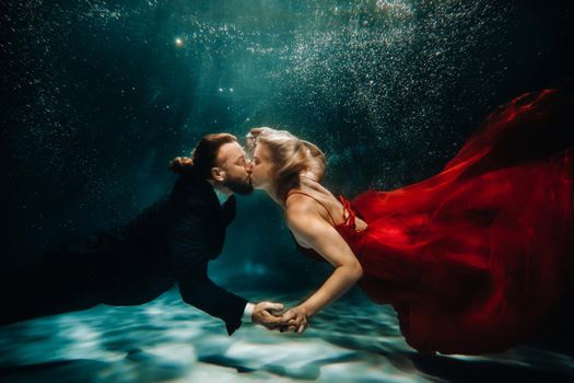 A woman in a red dress and a man in a suit are kissing underwater.A pair of floats under water.