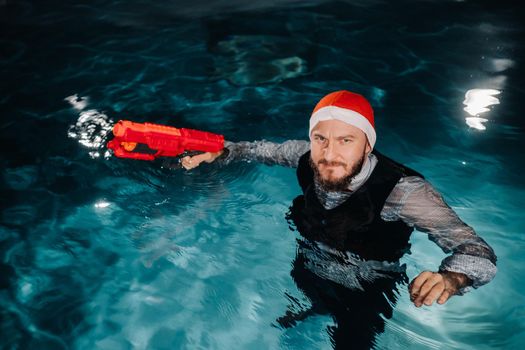 A man in a Santa Claus suit and hat with a red gun in his hands. Santa Claus is swimming underwater with a gun.Christmas concept