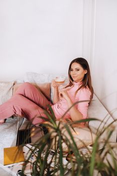 a girl in the morning in pajamas at home working on a laptop with drinking coffee, a girl self-isolated at home and resting on the couch and watching a laptop.Household chores.