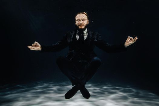 A man in a strict suit under water in the Lotus position.