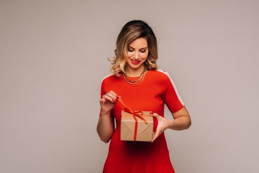 A girl in a red dress stands with gifts in her hands on a gray background.
