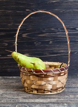 lying in a basket of green ripe pears, a basket stands on a black wooden table, closeup
