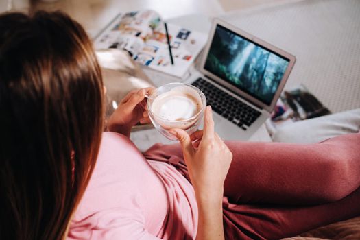 a girl in the morning in pajamas at home working on a laptop with drinking coffee, a girl self-isolated at home and resting on the couch and watching a laptop.Household chores.