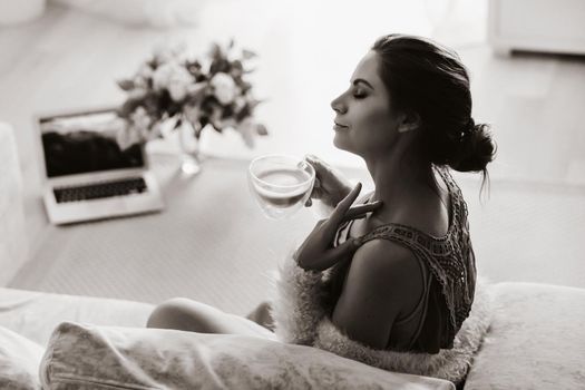 a relaxed girl at home drinks coffee and watches a movie.Domestic calm.The girl is sitting comfortably on the sofa and drinking coffee.black and white photo.