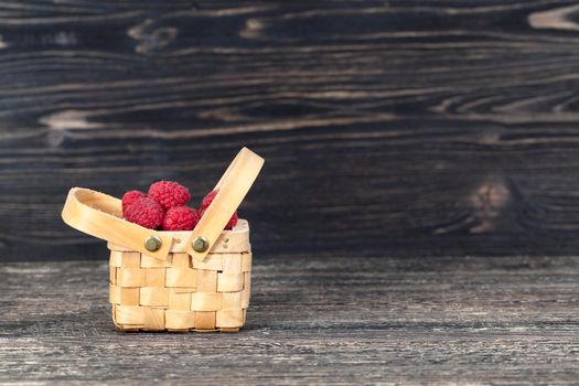 berries of red raspberries lying in a rough wooden basket, standing on a wooden table,
