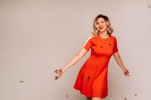 A girl in a red dress stands smiling on a white background.