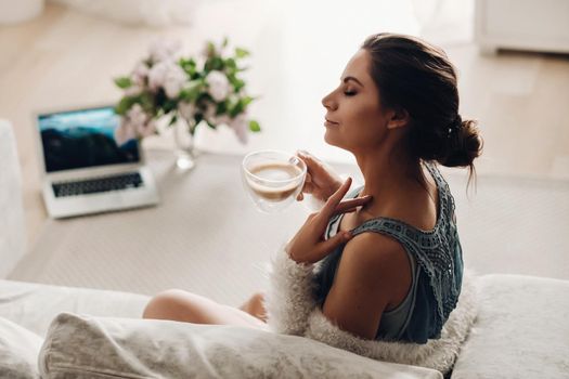 a relaxed girl at home drinks coffee and watches a movie.Domestic calm.The girl is sitting comfortably on the sofa and drinking coffee.