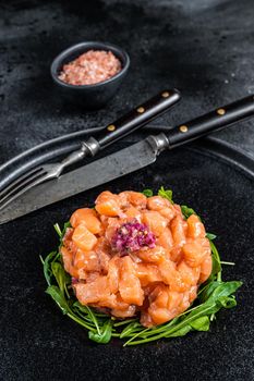 Raw Salmon tartare or tartar with red onion, arugula and capers in black plate. Black background. Top View.