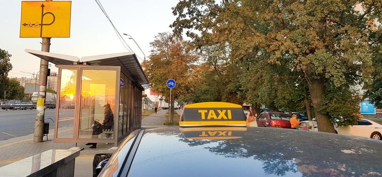 Light box checker taxi bright yellow on the roof of the car on a background of sky, city and people.