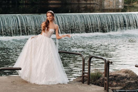 An elegant bride in a white dress and gloves stands by the river in the Park, enjoying nature.A model in a wedding dress and gloves in a nature Park.Belarus.