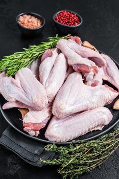 Raw duck wings on a plate with herbs. Black background. Top view.