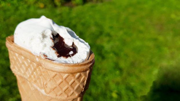 bitten ice cream in a waffle cup with chocolate filling. Bitten white ice cream with caramel on a background of green grass in summer.