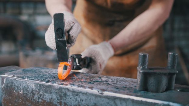 The blacksmith bends iron rod on the anvil with hammer, metal work, close up, telephoto