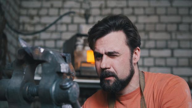 Blacksmith bends metal knife with gripe in workshop forge, portrait, telephoto