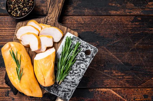 Sliced Smoked chicken breast fillet meat on a butcher board. Dark wooden background. Top view. Copy space.