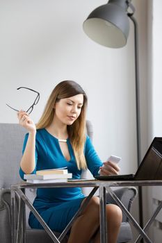 Fashionable business woman in office holds glasses and looking to smartphone, telephoto