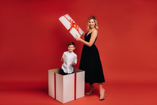 mom opens a huge Christmas gift in which a boy stands and shows the class on a red background.