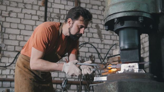 Man blacksmith in workshop forging red hot iron on anvil - small business, telephoto