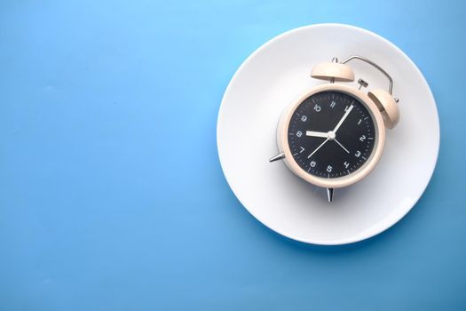 Alarm clock on plate on wooden table, top view