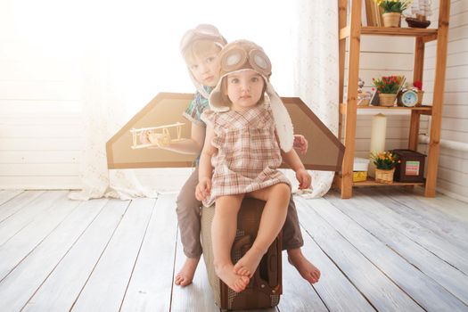 Happy children playing with vintage wooden airplane. Kids having fun at home. Imagination and freedom concept. Two little children wearing pilot costume and playing with old suitcase. .