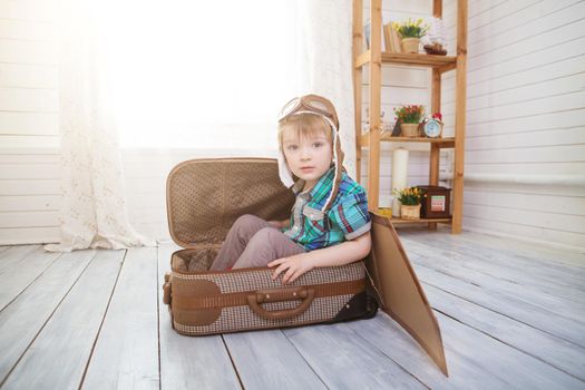 Little boy sits on a suitcase playing with model airplane. Fantasy travel concept. .