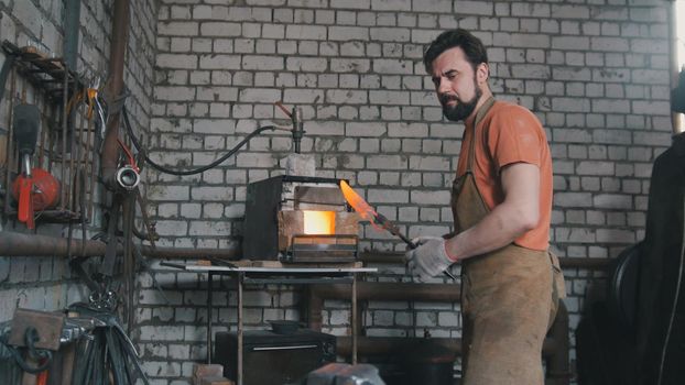 Young muscular man working on a blacksmith with metal, wide angle