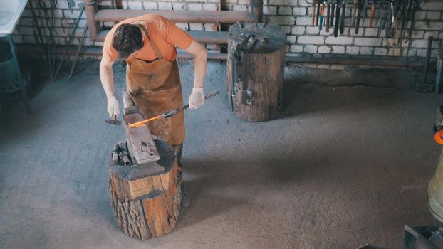 Beard man blacksmith in forge makes metal tools on iron anvil with hammer, top view, small business