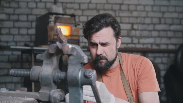 Blacksmith bends metal knife with gripe in workshop forge, portrait, telephoto