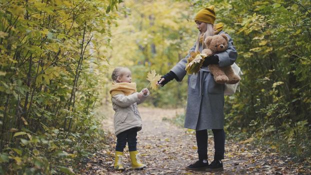 Mother and her daughter little girl walking in a autumn park - playing with Teddy Bear, telephoto