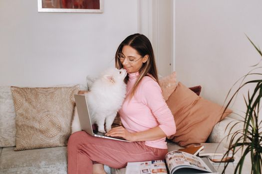 a girl in pajamas at home is working on a laptop with her dog Spitzer, the dog and its owner are resting on the couch and watching the laptop.Household chores.